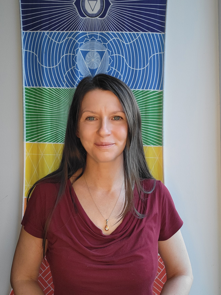 Person steht vor farbigem, geometrischem Wandtuch und lächelt in die Kamera